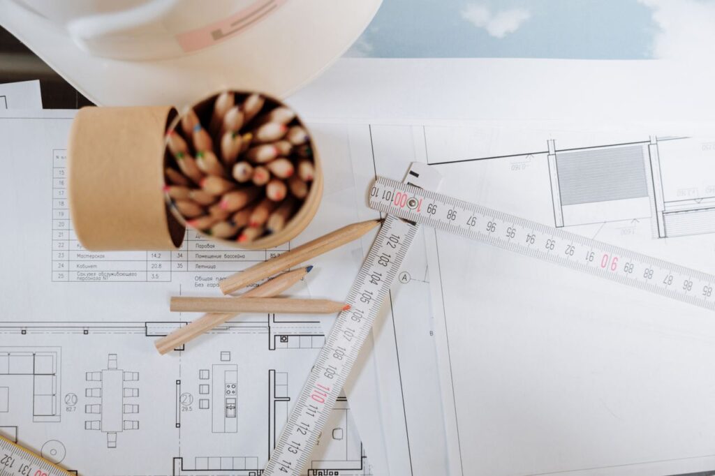 Colorful pencils and ruler atop architectural blueprints on a workspace.
