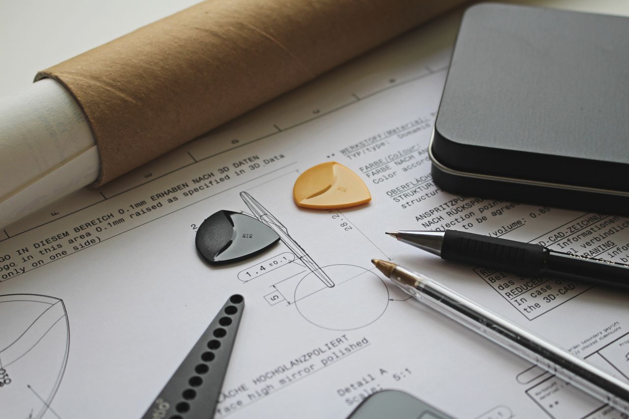 A technical engineering draft with guitar picks, pens, and a roll of paper showcasing precision and creativity.